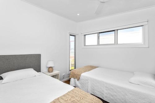 two beds in a white room with two windows at Pas Beach House Apartment 2 in Mollymook