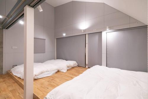 two beds in a room with white walls and wood floors at Social Guest House neltoko in Nanao