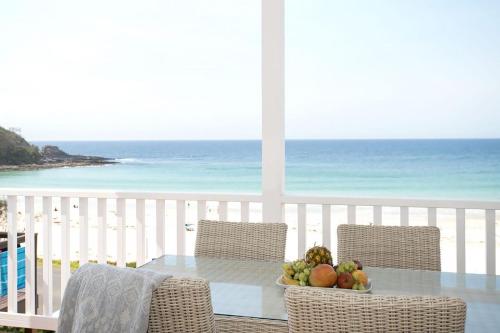 a table with a bowl of fruit on a balcony with the beach at Pas Beach House Apartment 1 in Mollymook