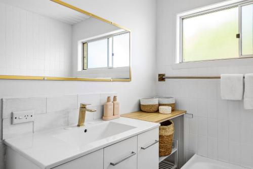 a white bathroom with a sink and a mirror at Coast House Mollymook in Mollymook