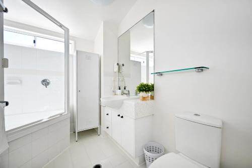 a white bathroom with a toilet and a sink at Beachfront Choices - Beach, Lagoon, Spa ZE1 in Alexandra Headland