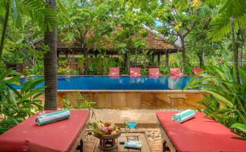 um resort com uma piscina e mesas e cadeiras vermelhas em Pandora Suite D'Angkor em Siem Reap