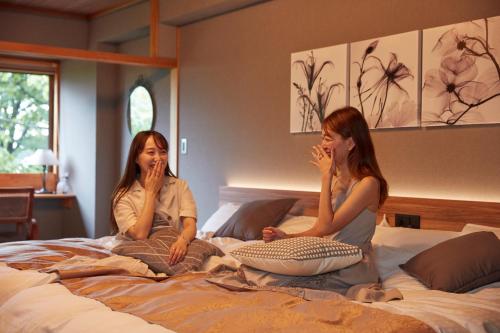 two women sitting on top of a bed at Towadakohan Sakura in Towada