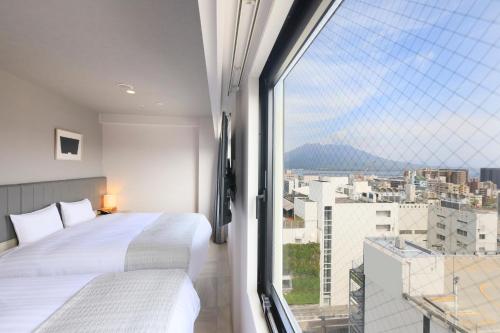 een slaapkamer met 2 bedden en een groot raam bij QuintessaHotel KagoshimaTenmonkan Relax&Sleep in Kagoshima