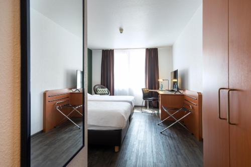 a hotel room with a bed and a desk and a mirror at ACHAT Hotel Heppenheim in Heppenheim an der Bergstrasse