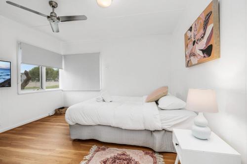 a white bedroom with a bed and a table at Coastal Cottage Batemans Bay in Batemans Bay