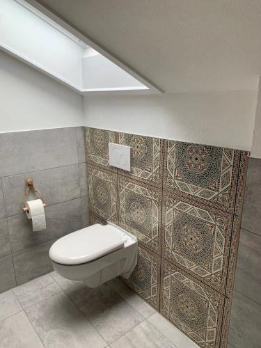 a bathroom with a toilet and a tile wall at Ferienwohnungen mama ELVA in Leutkirch im Allgäu