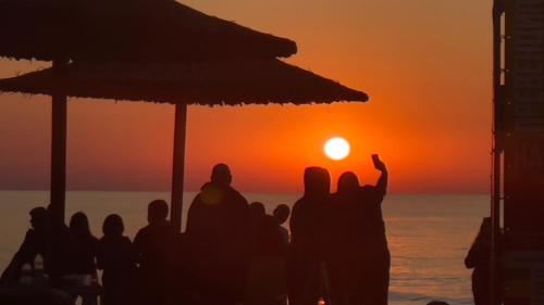 um grupo de pessoas de pé na praia assistindo o pôr do sol em Family Hotel Morska Zvezda em Balchik