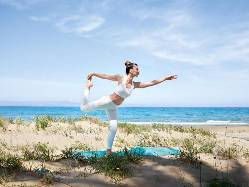 a woman is standing on a yoga mat on the beach at Grecotel LUXME Palms at Riviera Olympia & Aqua Park in Loutra Killinis