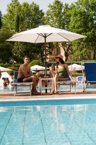 a man and woman sitting under an umbrella next to a pool at Grand Hotel Telese in Telese