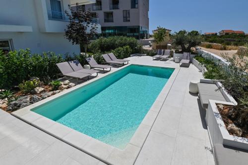 a swimming pool with chaise lounges and chairs next to a building at VILLA CALA, Hotel Rooms&Apartments in Novalja