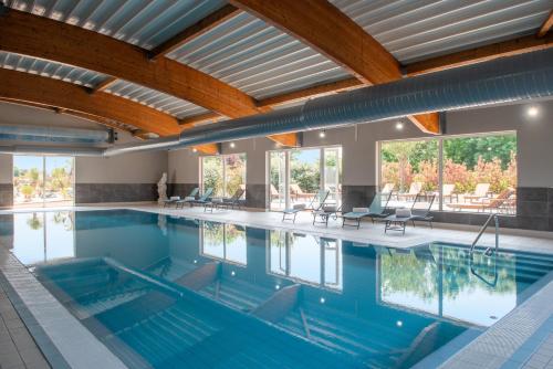 uma grande piscina com água azul e tectos de madeira em Golden Tulip Dieppe Hôtel & Spa em Saint-Aubin-sur-Scie