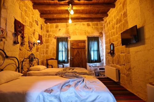 a bedroom with two beds and a tv in a stone wall at Nova Cave Hotel in Ortahisar