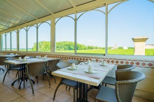 un comedor con mesas, sillas y ventanas en Hôtel de Margaux, en Margaux