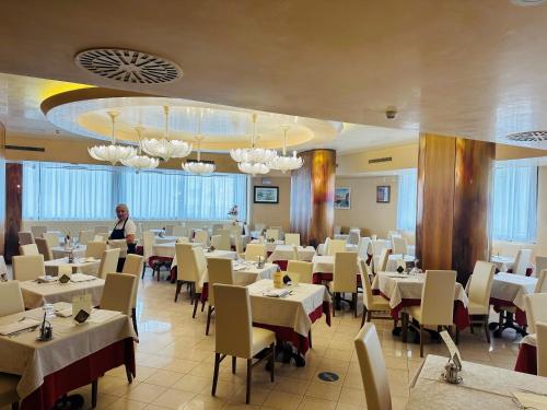 ein Esszimmer mit weißen Tischen und Stühlen und einem Mann in der Unterkunft Hotel Kennedy in Bibione