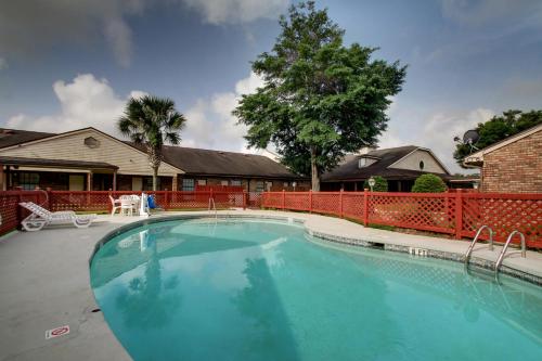 a large swimming pool in a yard with a red fence at HOTEL DEL SOL - Pensacola in Pensacola