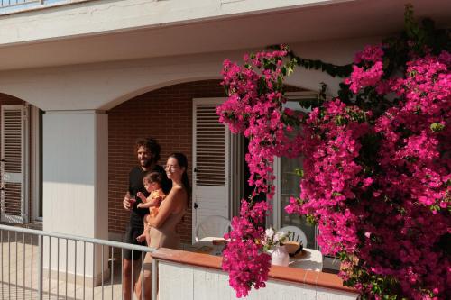 a man and woman holding a baby on a balcony with pink flowers at I Cinque Pini in Follonica