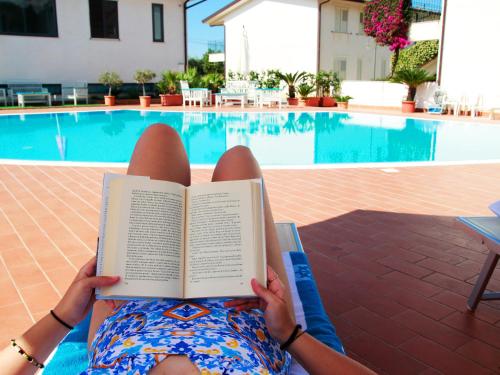 a woman reading a book in front of a swimming pool at Medimare Residence Club in Patti
