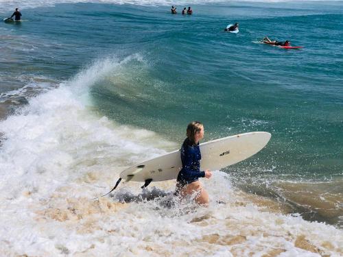 a woman walking into the ocean with a surfboard at Star Rest Beach Hotel in Arugam Bay