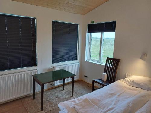 a bedroom with a bed and a table and two windows at Gaukshof in Selfoss