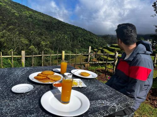 un hombre sentado en una mesa con comida y zumo de naranja en Queenmary cottages, en Nanu Oya
