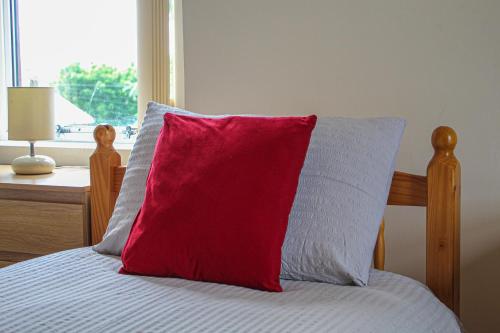 a red pillow sitting on top of a bed with a window at Lotus Studio near Lanark in Carstairs