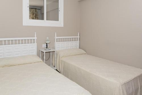 two beds in a white room with a mirror at Mar Y Montaña 7º-119 in Cullera