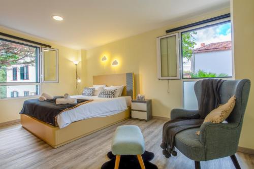 a bedroom with a bed and a chair and windows at Mateus House - Porto da Cruz Center in Porto da Cruz
