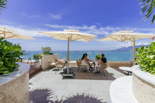 zwei Personen sitzen an einem Tisch unter Sonnenschirmen in der Unterkunft Grand Hyams Hotel - Quy Nhon Beach in Quy Nhon