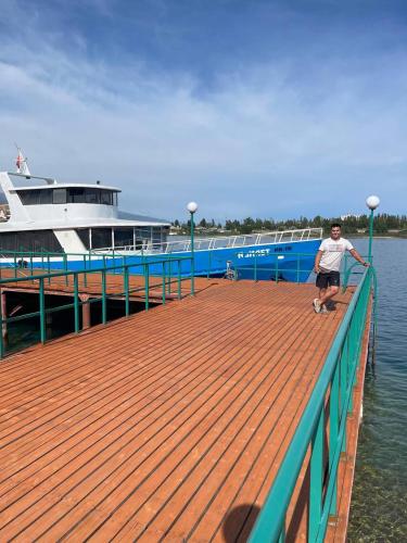 チョルポン・アタにあるБухта гостевой домの船の横の桟橋に立つ男