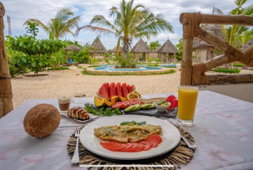 un tavolo con un piatto di cibo e un bicchiere di succo d'arancia di Haber Hotel & SPA a Matemwe