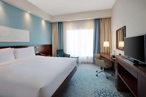 a hotel room with a bed and a desk and a television at Hampton By Hilton Dubai Al Barsha in Dubai