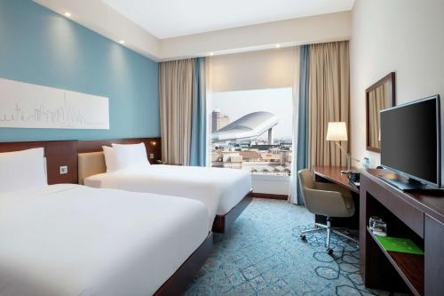 Hampton By Hilton Dubai Al Barsha في دبي: غرفة فندقية بسريرين وتلفزيون بشاشة مسطحة