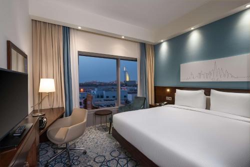 Hampton By Hilton Dubai Al Barsha في دبي: غرفه فندقيه بسرير ومكتب ونافذه