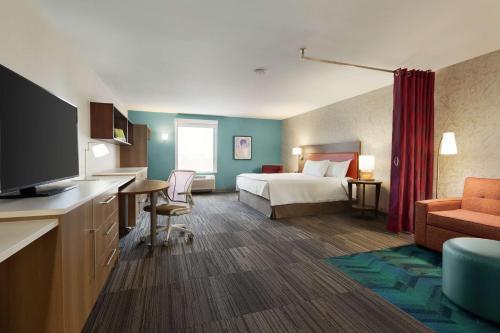 a hotel room with a bed and a desk with a television at Home2 Suites By Hilton Portland Airport in Portland