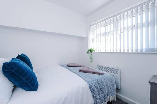 a white bed with blue pillows and a window at Beautiful apartment tres - free public parking in Litherland