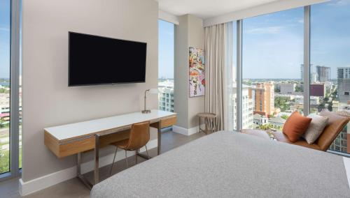 a hotel room with a desk and a tv on a wall at Canopy West Palm Beach - Downtown in West Palm Beach