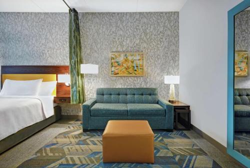 Habitación de hotel con cama y sofá azul en Home2 Suites By Hilton Lawrenceville Atlanta Sugarloaf, Ga en Lawrenceville