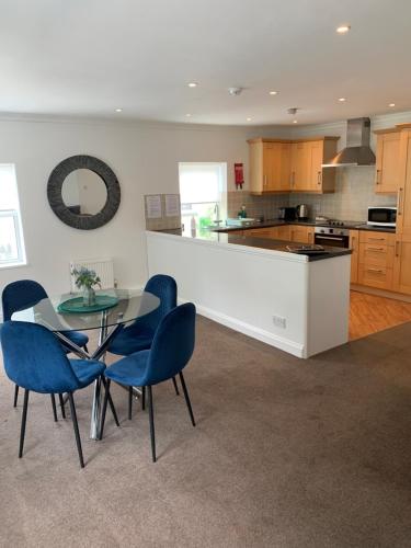 a kitchen with a glass table and blue chairs at The Apartment, Bridge House in Laxey