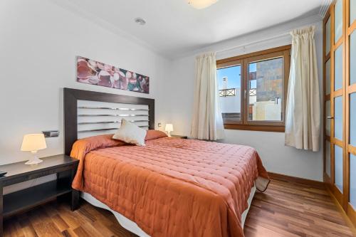 a bedroom with a bed with an orange bedspread and a window at Siesta Suites Lanzarote in Yaiza