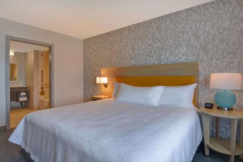 a hotel room with a large bed and a hallway at Home2 Suites Williston Burlington, Vt in Williston