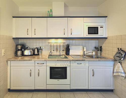 eine Küche mit weißen Schränken, einer Spüle und einer Mikrowelle in der Unterkunft Haus Ferienidyll in Ahlbeck
