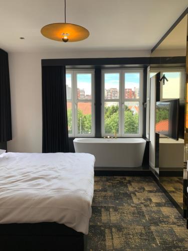 1 dormitorio con cama, bañera y ventanas en Bed & Breakfast Maison Noire Westende-bad incl parking & ontbijt, en Middelkerke