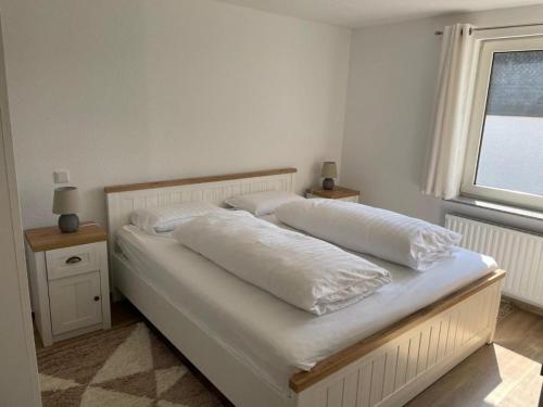 Cama blanca con almohadas blancas y ventana en Ferienwohnung KORS en Winterberg