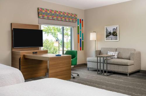 a hotel room with a bed and a television and a chair at Hampton Inn & Suites Raleigh Midtown, NC in Raleigh