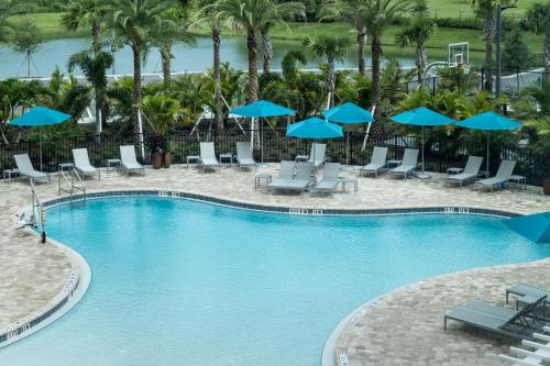 a swimming pool with chairs and blue umbrellas at Home2 Suites By Hilton Cape Canaveral Cruise Port in Cape Canaveral