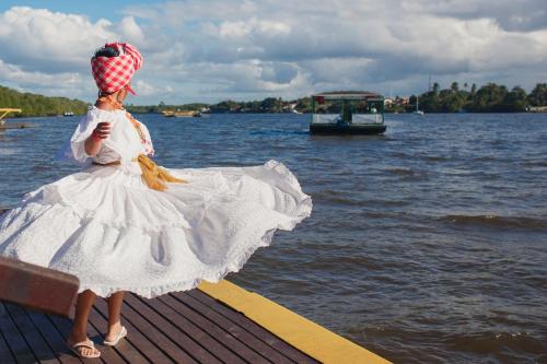 a woman in a white dress standing on a dock near the water at Transamerica Comandatuba - All Inclusive Resort in Ilha de Comandatuba