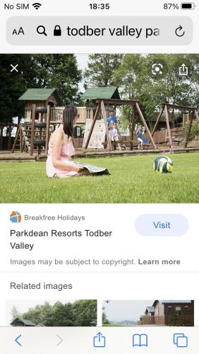 a woman sitting on the grass in front of a playground at Cliffs caravan hire in Gisburn