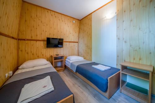 two beds in a room with wooden walls and a tv at OW Gromada Pod Bukami in Międzyzdroje