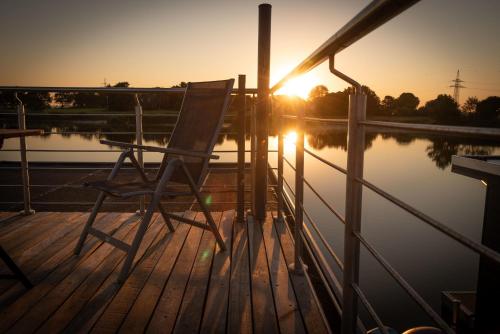 a chair sitting on a dock with the sunset at Hausboot Wangermeer Nordsonne11 in Wangerland